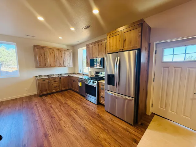 Kitchen with stainless steel appliances, dark wood-style flooring, light stone countertops, recessed lighting, and wood finish cabinets