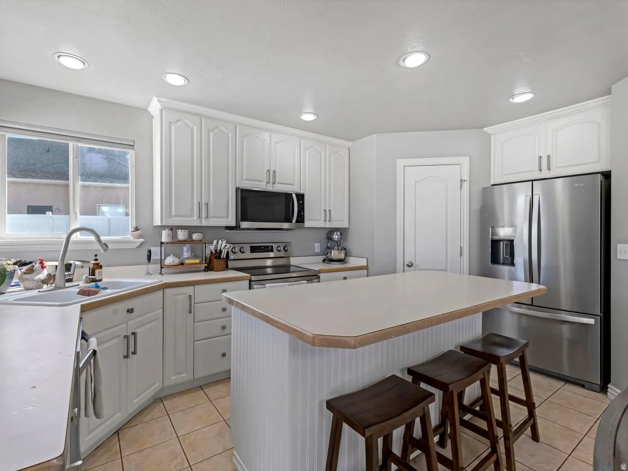 Kitchen with light countertops, white cabinetry, stainless steel appliances, a breakfast bar, and a kitchen island