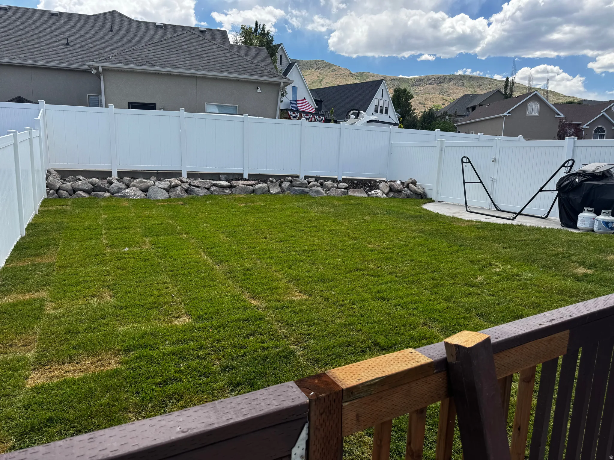 Expansive backyard featuring a lush lawn, white privacy fencing, a natural rock border, and a concrete patio section