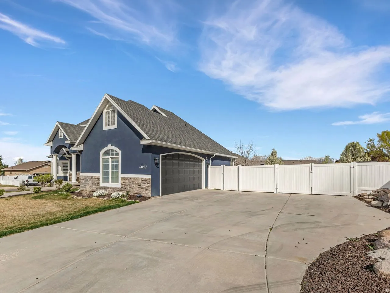 View of side of property featuring stucco siding, stone siding, a gate, an attached garage, and concrete driveway