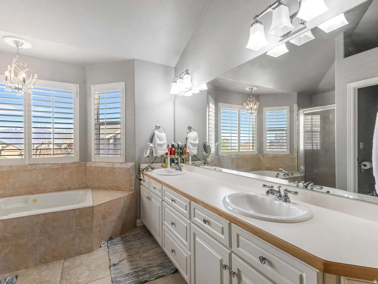 Bathroom featuring a bath, suspended lighting, lofted ceiling, a stall shower, and double vanity