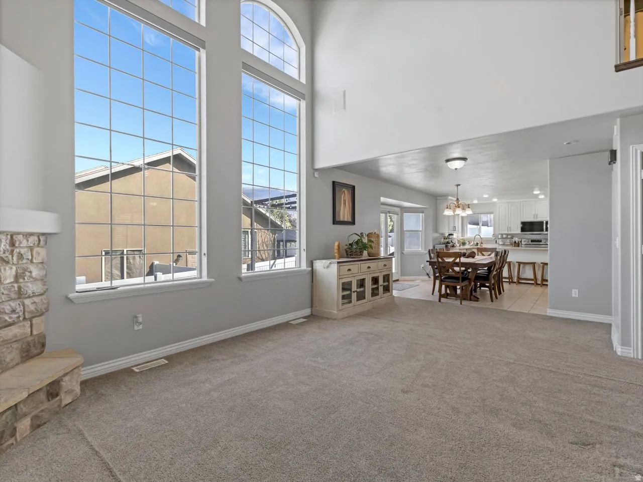 Living room with light colored carpet, a high ceiling, and suspended lighting