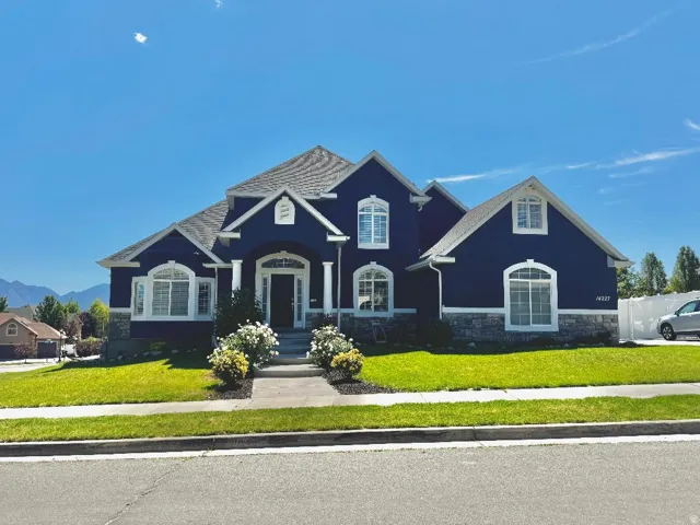Two-story residence featuring a dark blue exterior with white trim, a gabled roofline, and a stone foundation