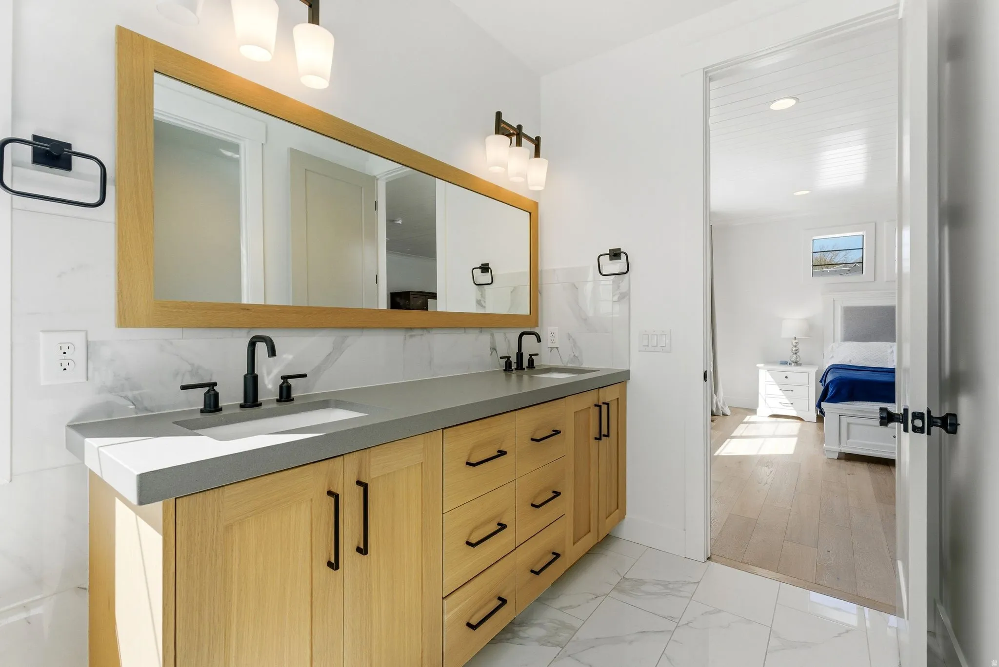 Primary Bedroom Ensuite bathroom with double vanity, light marble finish floors, and decorative backsplash