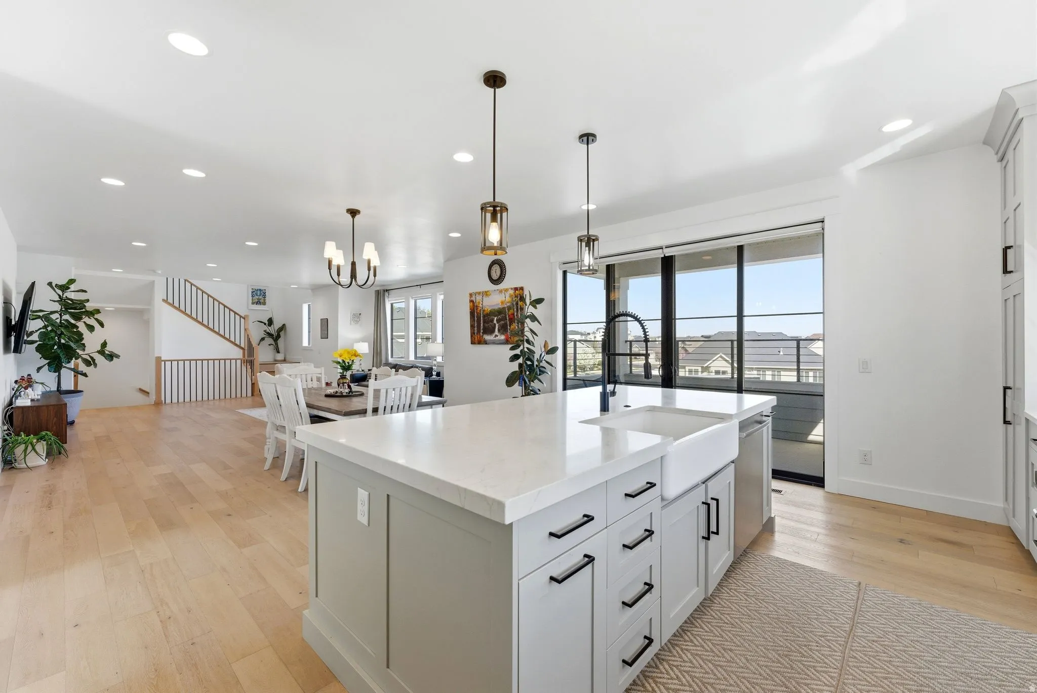 Kitchen featuring light wood finished floors, light stone countertops, a center island with sink, white cabinetry, and open floor plan