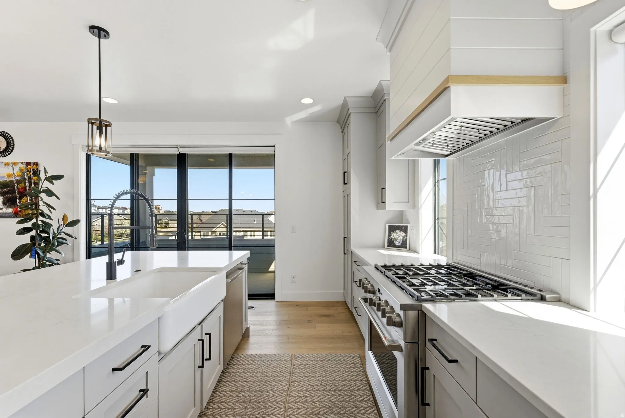 Kitchen & front balcony featuring stainless steel range, decorative light fixtures, light stone countertops, light wood finished floors, and tasteful backsplash