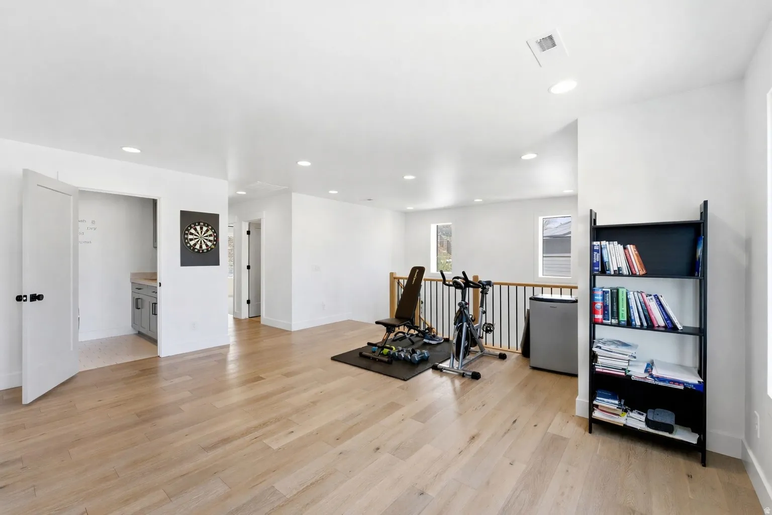 Exercise room with light wood-style floors and recessed lighting