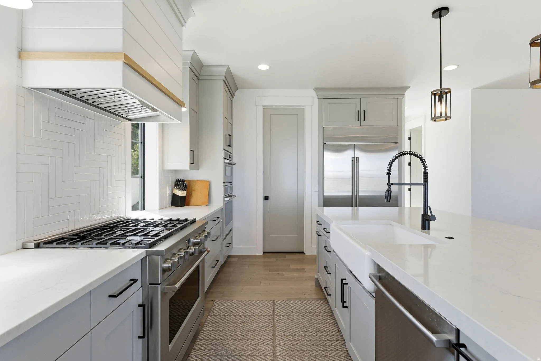 Kitchen pantry with gray cabinetry, stainless steel appliances, decorative light fixtures, light stone counters, and light wood finished floors