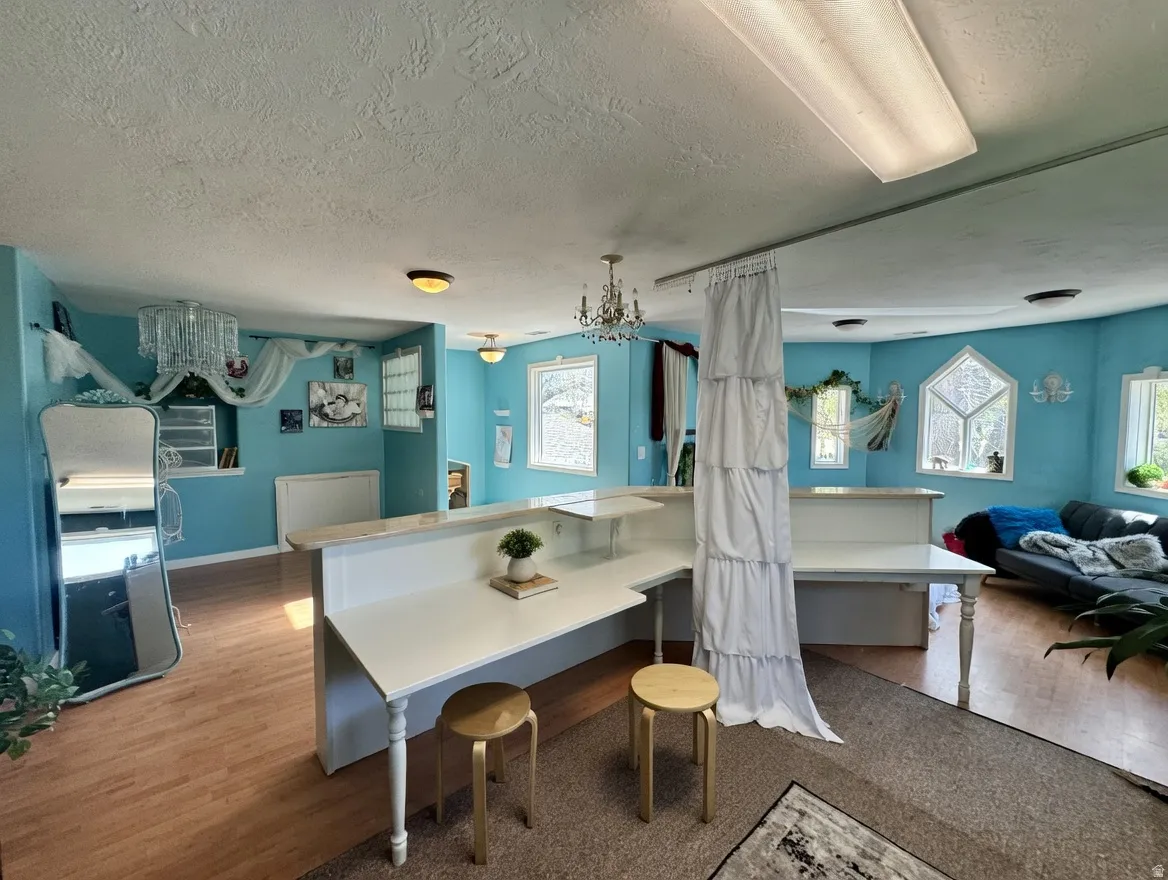 Kitchen with a textured ceiling, suspended lighting, wood finished floors, and a breakfast bar area