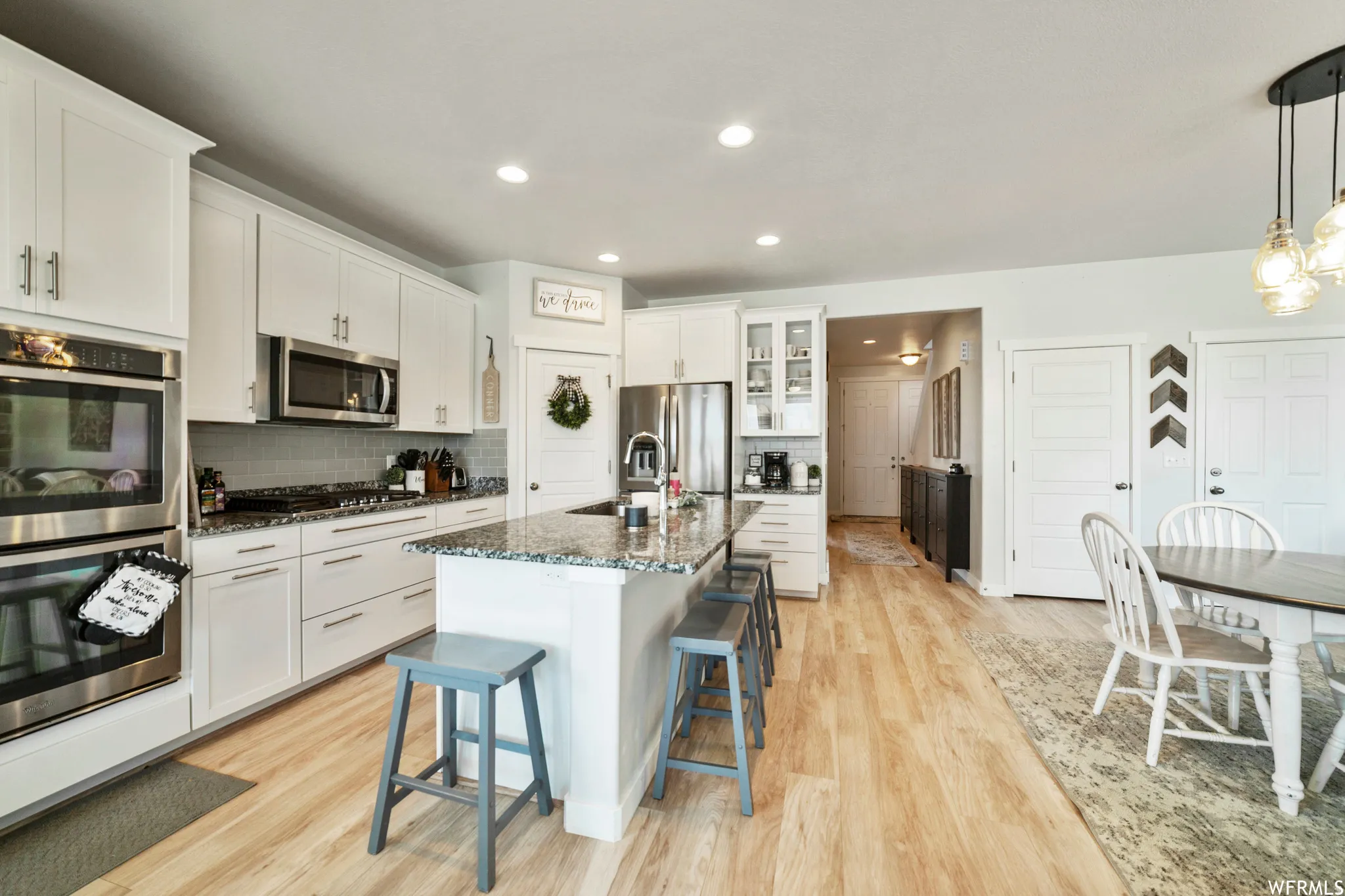 Kitchen with stainless steel appliances, dark stone countertops, a breakfast bar area, light wood-style flooring, and a kitchen island with sink