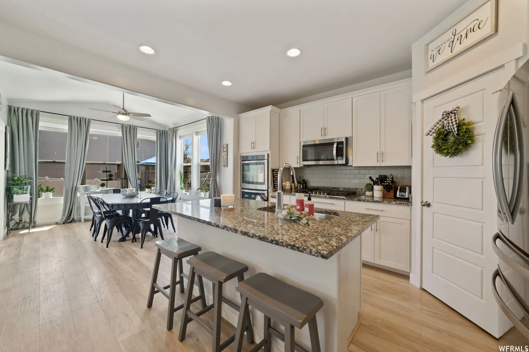 Kitchen featuring a breakfast bar area, light wood-style floors, stainless steel appliances, dark stone countertops, and recessed lighting