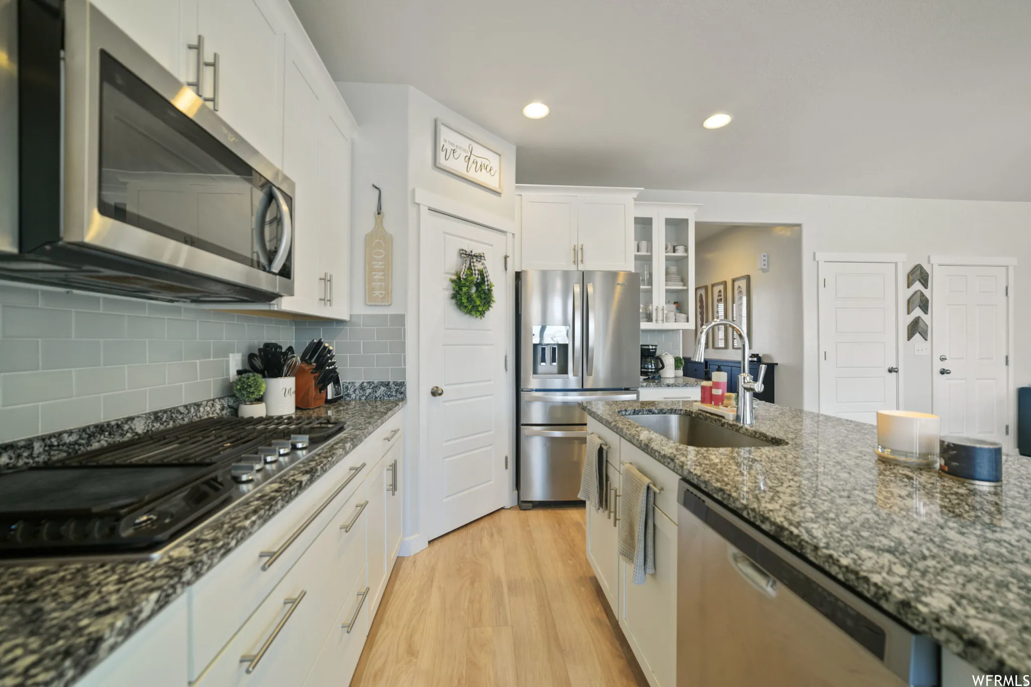 Kitchen featuring stainless steel appliances, light wood-style floors, white cabinetry, glass insert cabinets, and dark stone countertops