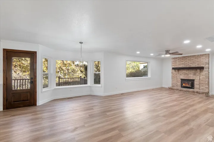 Unfurnished dining/family room featuring light wood-style floors, hanging lights, ceiling fan, and a brick fireplace
