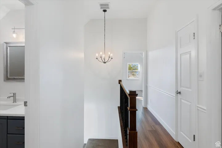 Hall with dark wood-style flooring, suspended lighting, and an upstairs landing