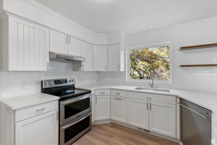 Kitchen featuring stainless steel appliances, open shelves, light wood-type flooring, white cabinetry, and ornamental molding