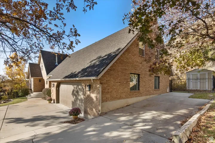 View of home's exterior with brick siding, a shingled roof, driveway, and a storage unit