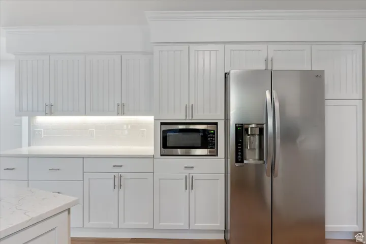 Kitchen featuring stainless steel appliances, white cabinets, backsplash, crown molding, and light stone countertops