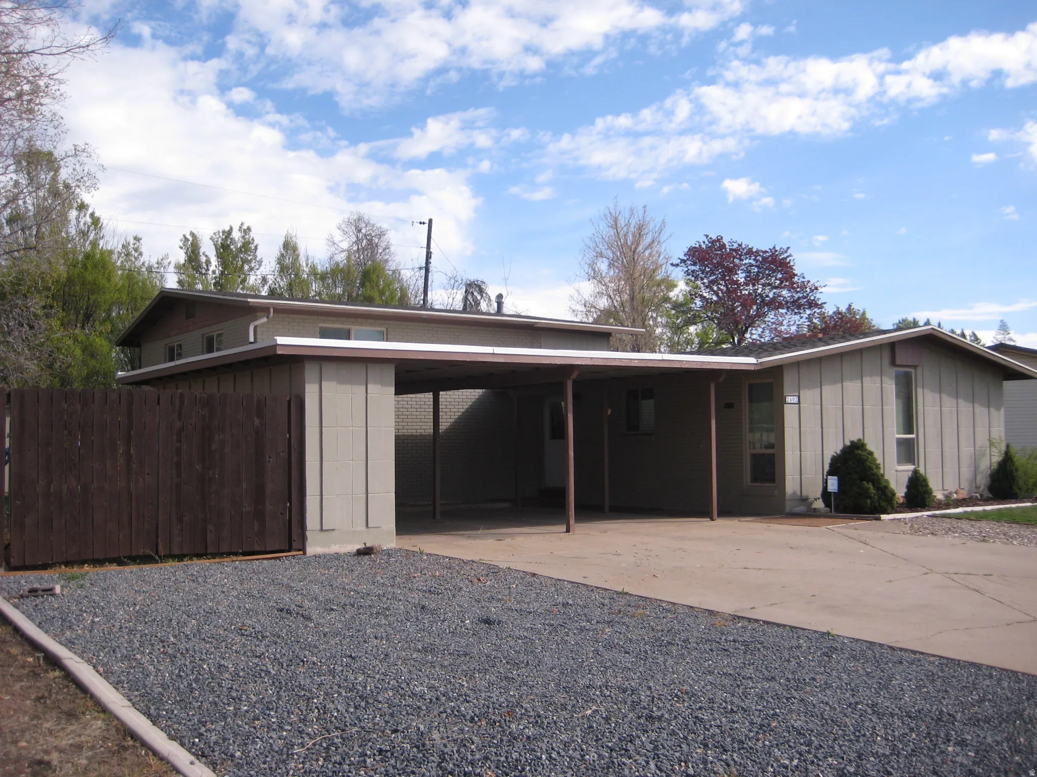View of front of house featuring board and batten siding, a carport, driveway, and brick siding