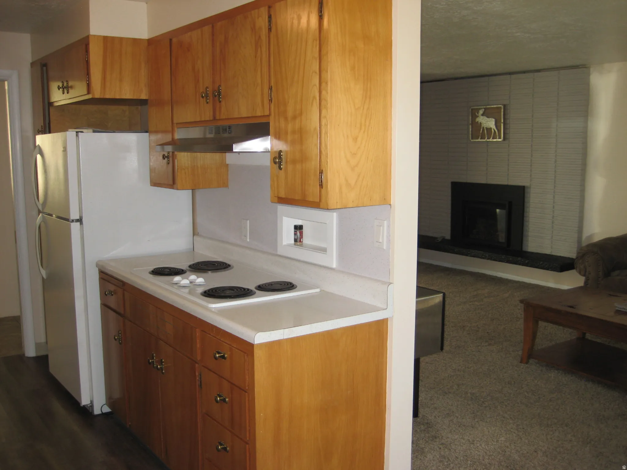 Kitchen with a brick fireplace, light countertops, wood finish cabinetry, a textured ceiling, and white electric stovetop