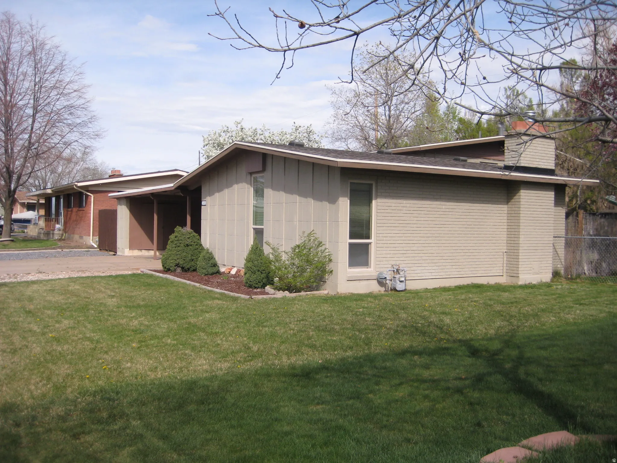 View of property exterior with a chimney, driveway, board and batten siding, a carport, and brick siding