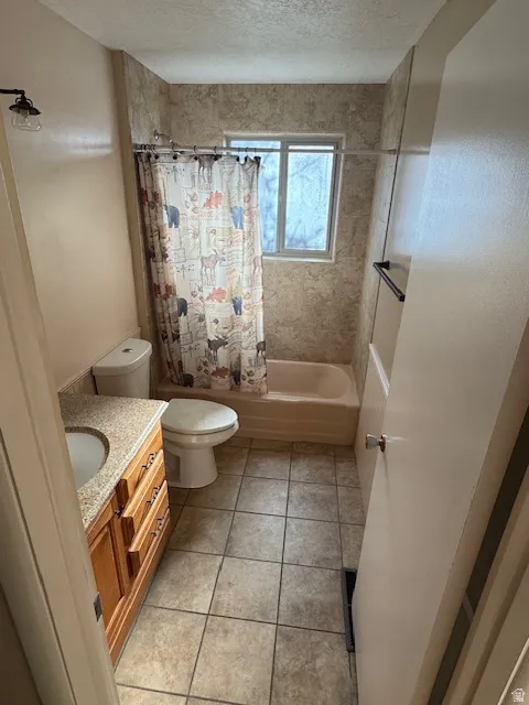 Bathroom with vanity, shower / bathtub combination with curtain, light tile patterned flooring, and a textured ceiling
