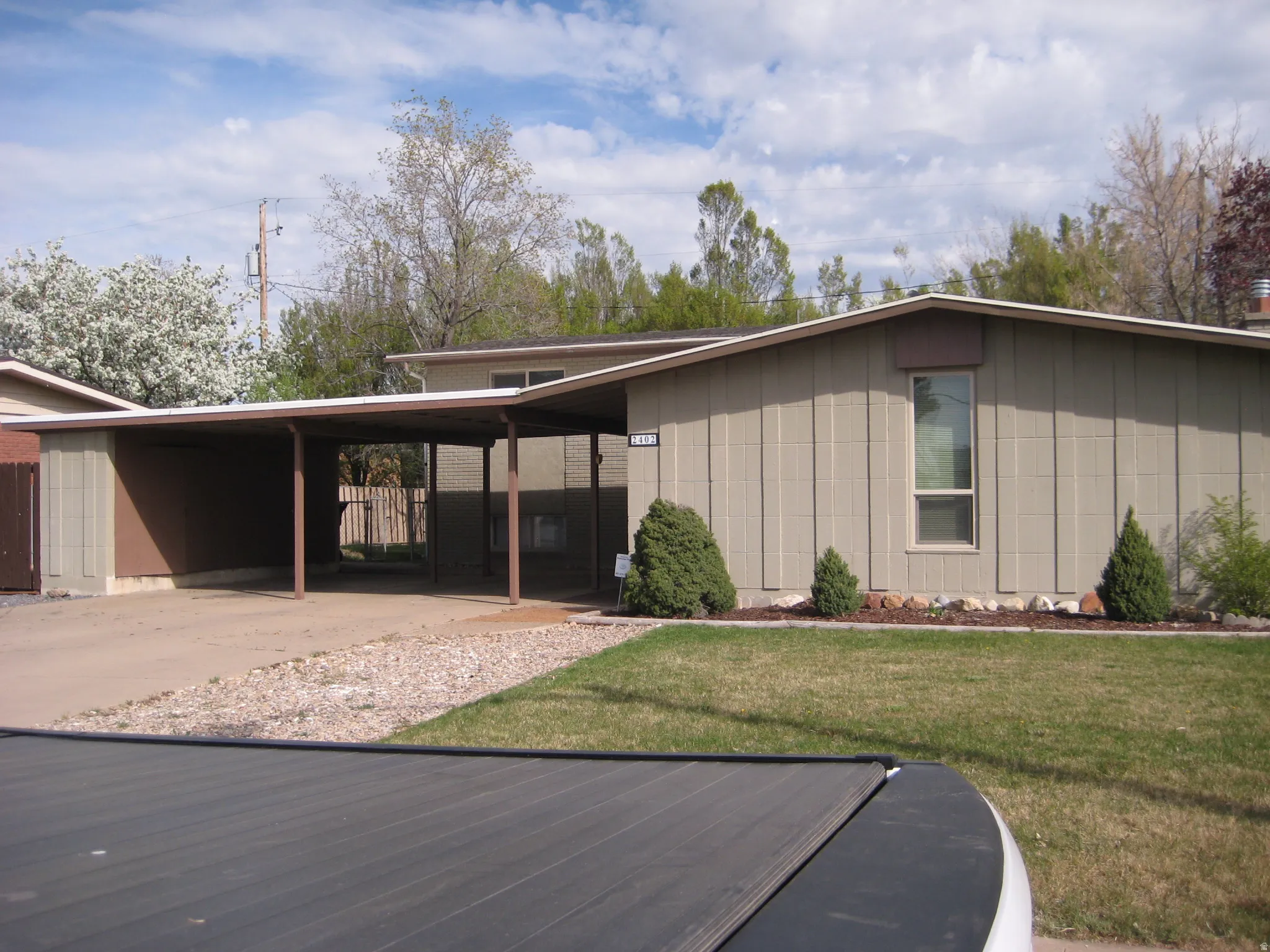 View of front facade featuring an attached carport, a front lawn, and driveway