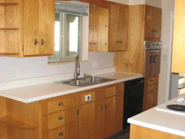 Kitchen with light countertops, wood finish cabinetry, open shelves, and dishwasher