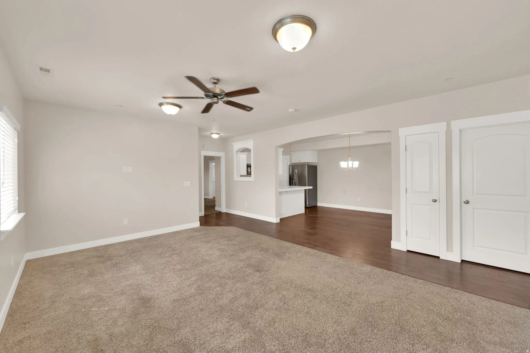 Unfurnished living room featuring dark carpet, ceiling fan, and arched walkways