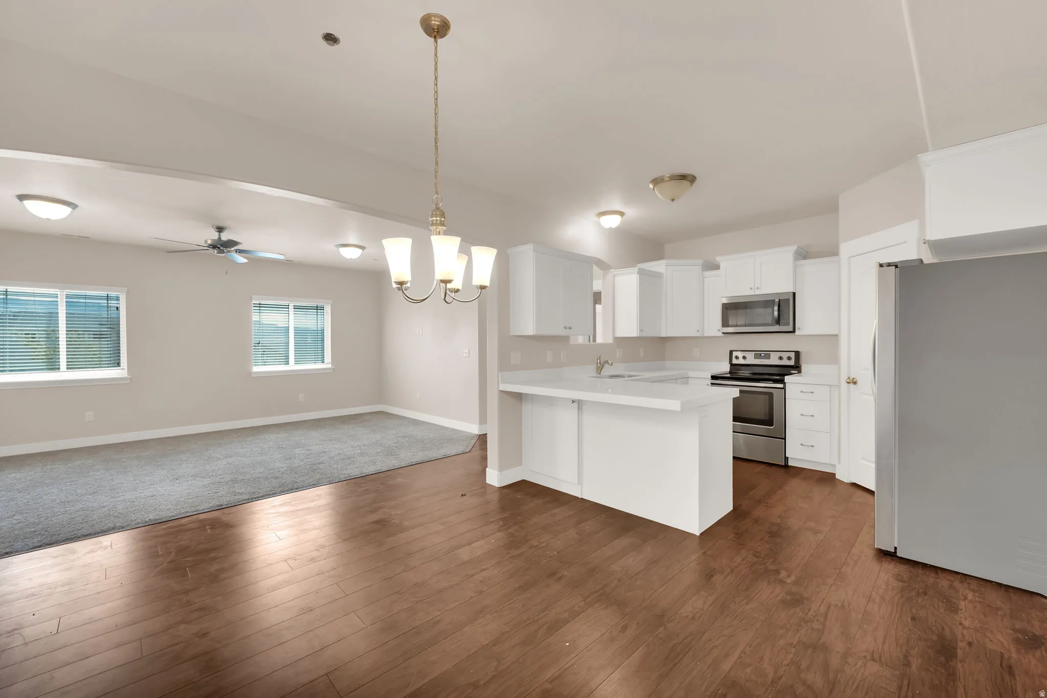 Kitchen with open floor plan, hanging lights, stainless steel appliances, light countertops, and a peninsula