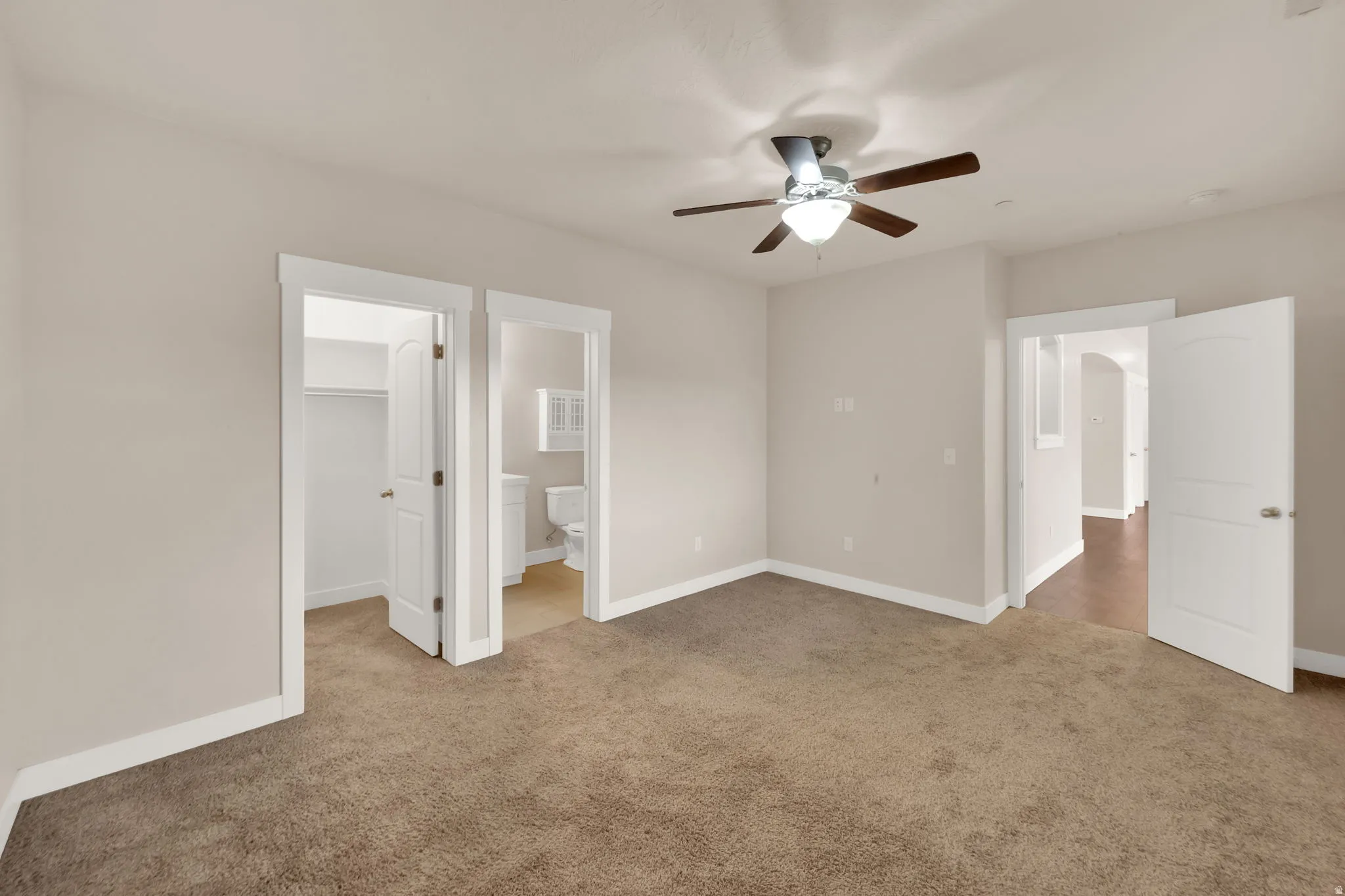 Unfurnished bedroom with a spacious closet, light colored carpet, a ceiling fan, and ensuite bath