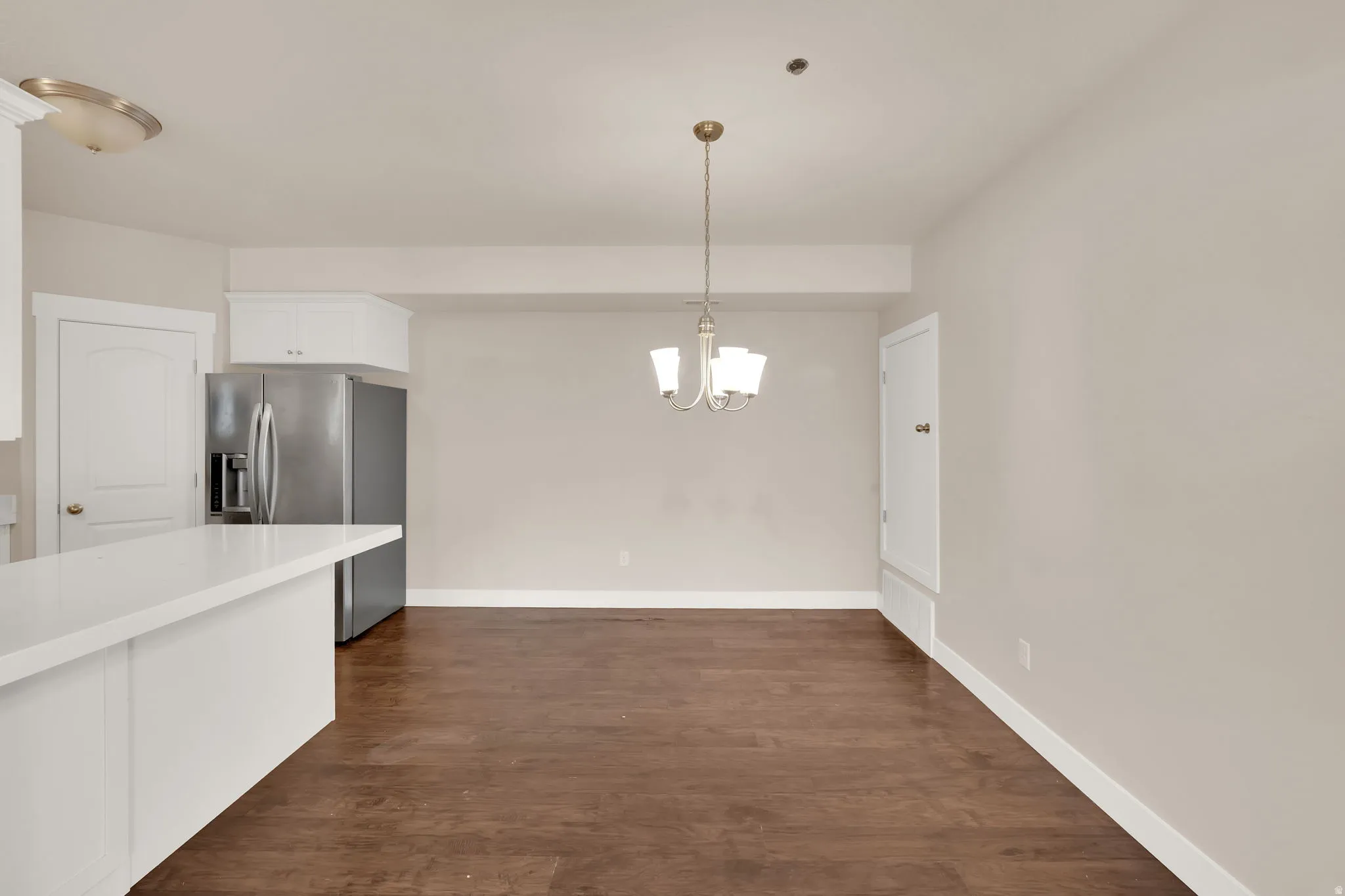 Kitchen featuring white cabinets, stainless steel fridge, dark wood finished floors, and suspended lighting