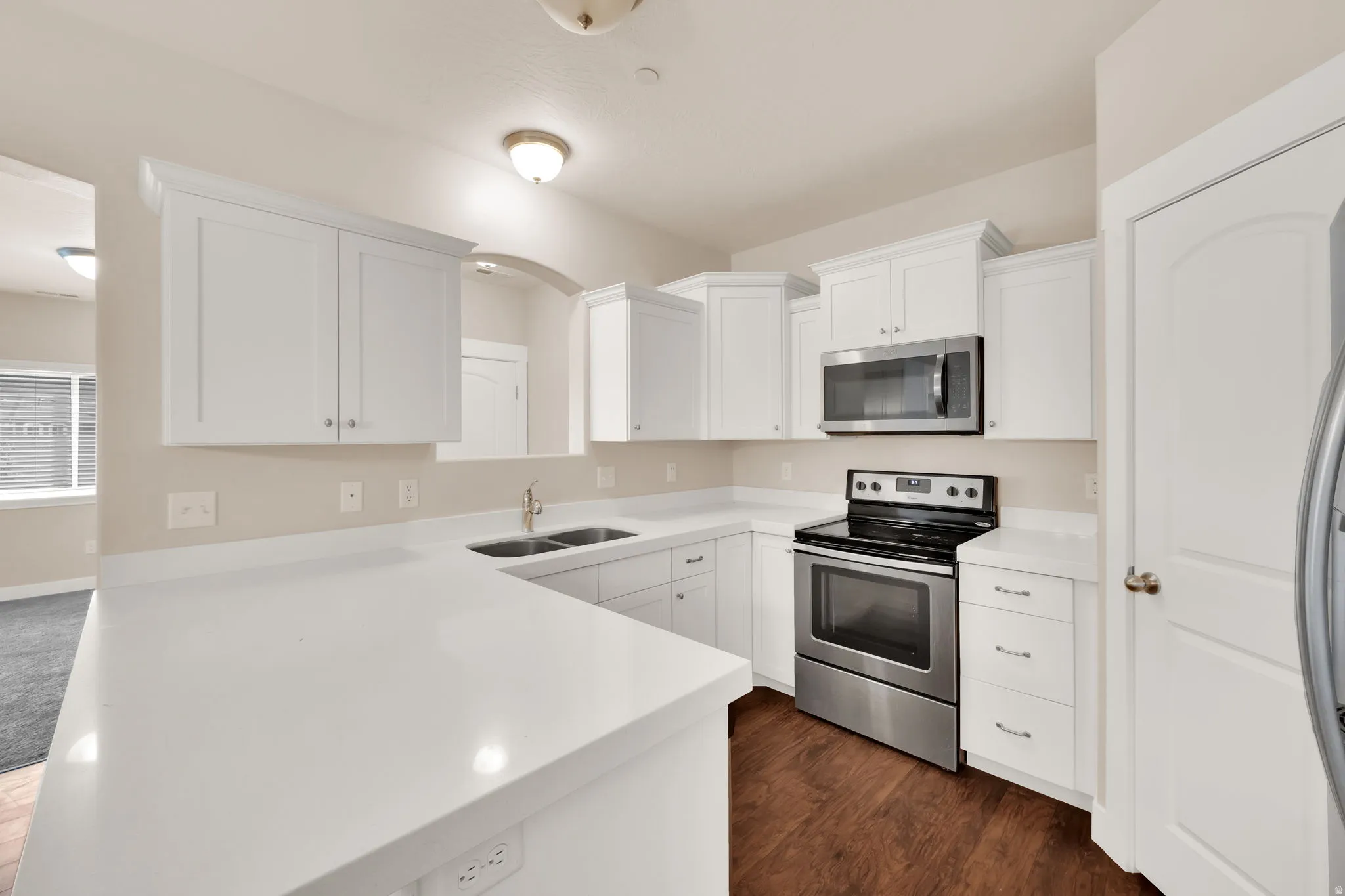 Kitchen featuring stainless steel appliances, white cabinetry, light countertops, dark wood-type flooring, and a peninsula
