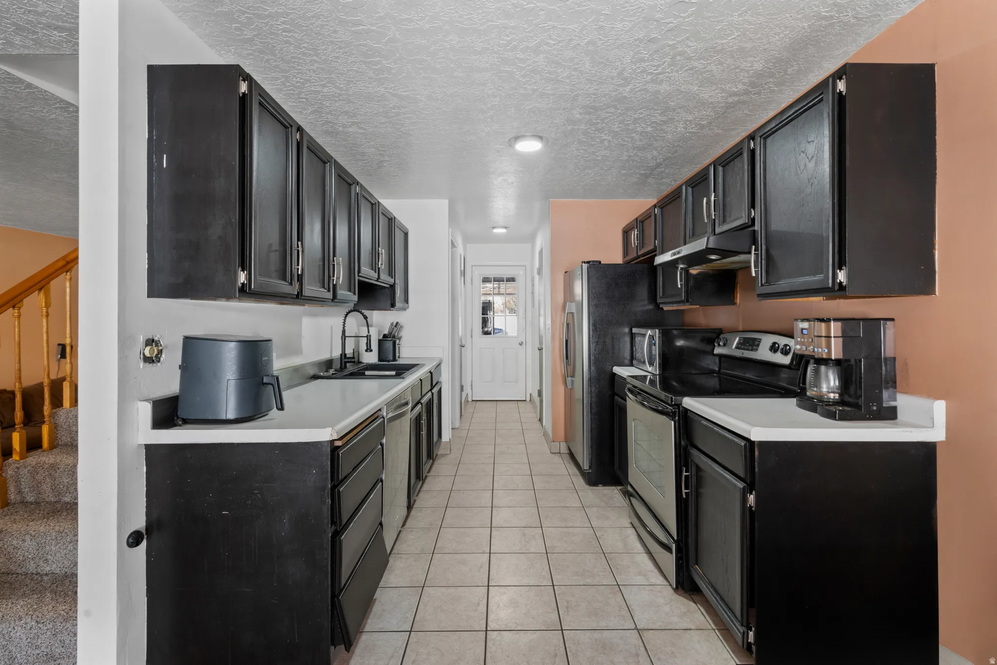 Kitchen with dark cabinetry, stainless steel appliances, light countertops, a textured ceiling, and light tile patterned flooring