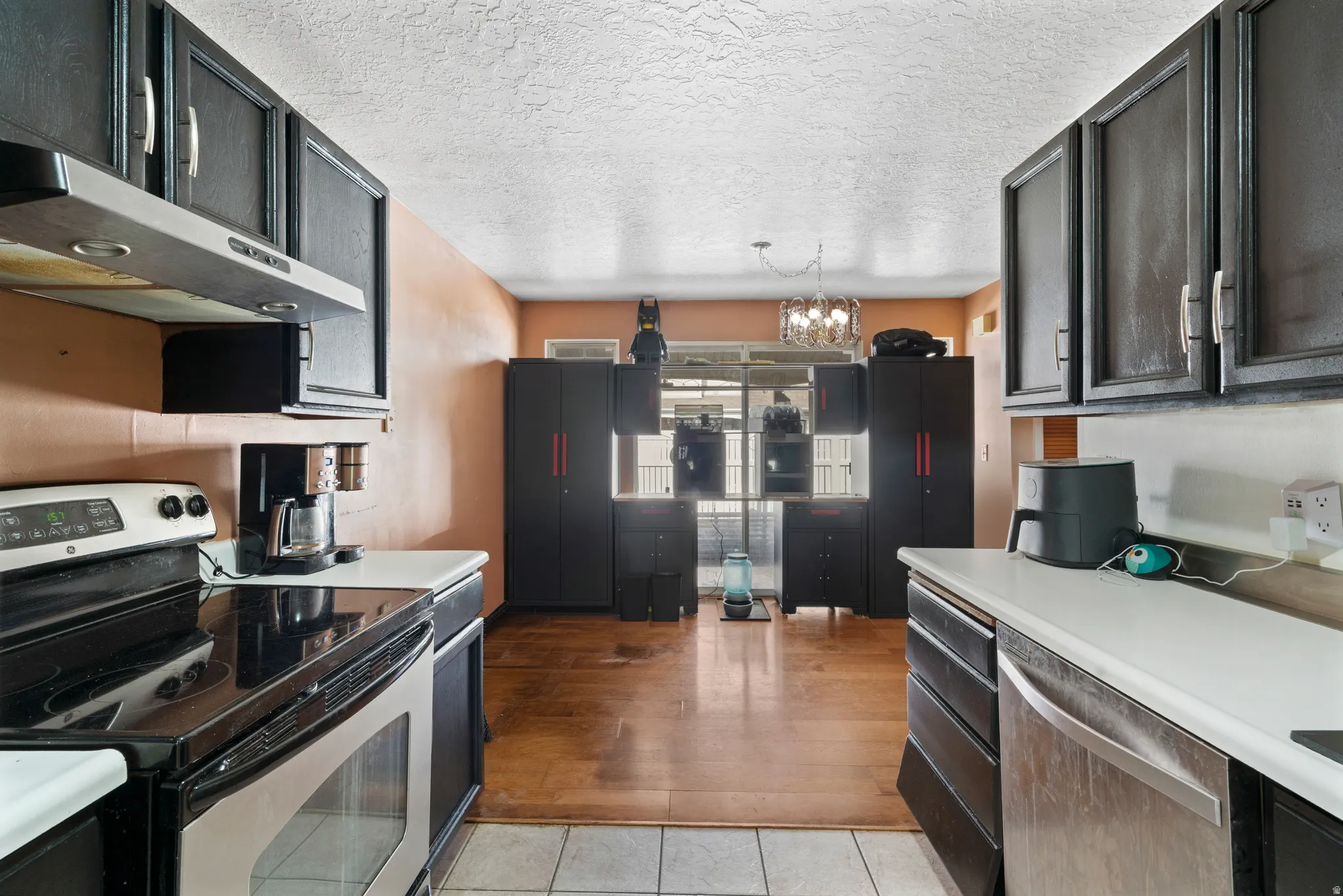 Kitchen with stainless steel appliances, light countertops, a textured ceiling, suspended lighting, and dark cabinetry