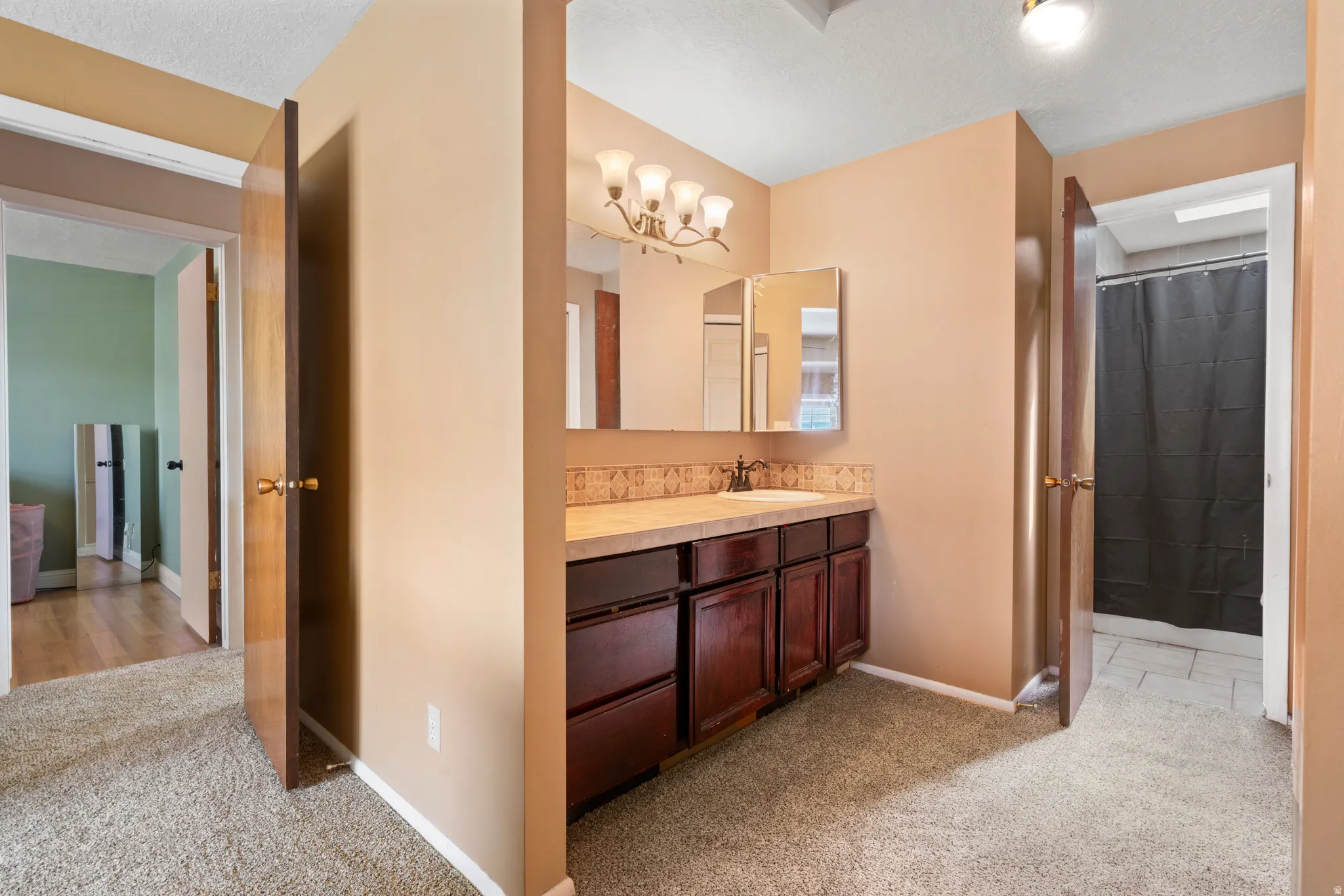 Master bedroom leading into bathroom with light carpet, vanity, curtained shower, and a textured ceiling
