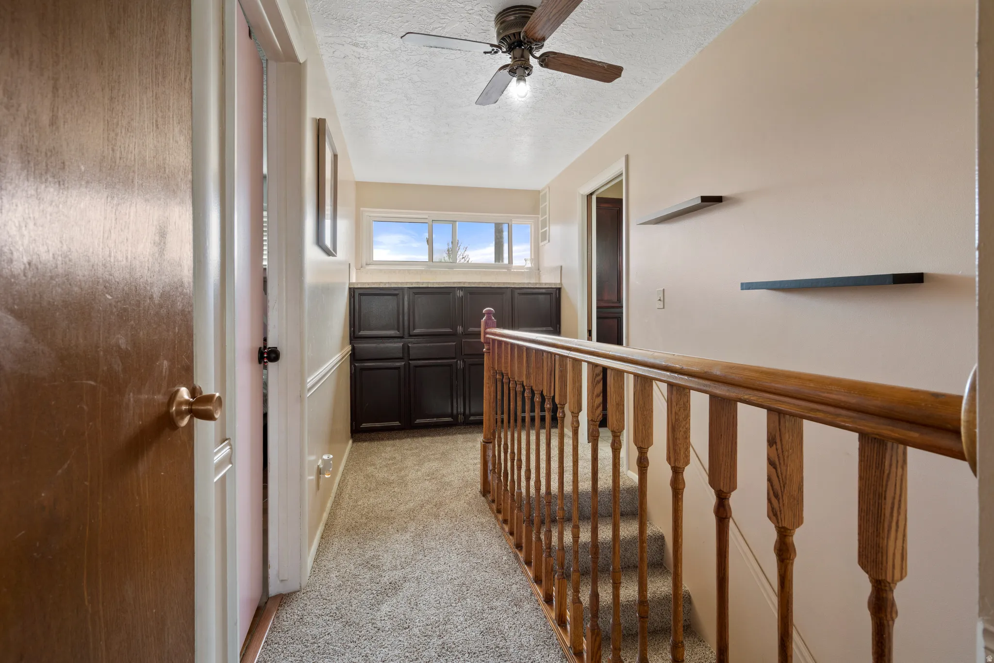 Hall featuring a textured ceiling, light colored carpet, and an upstairs landing
