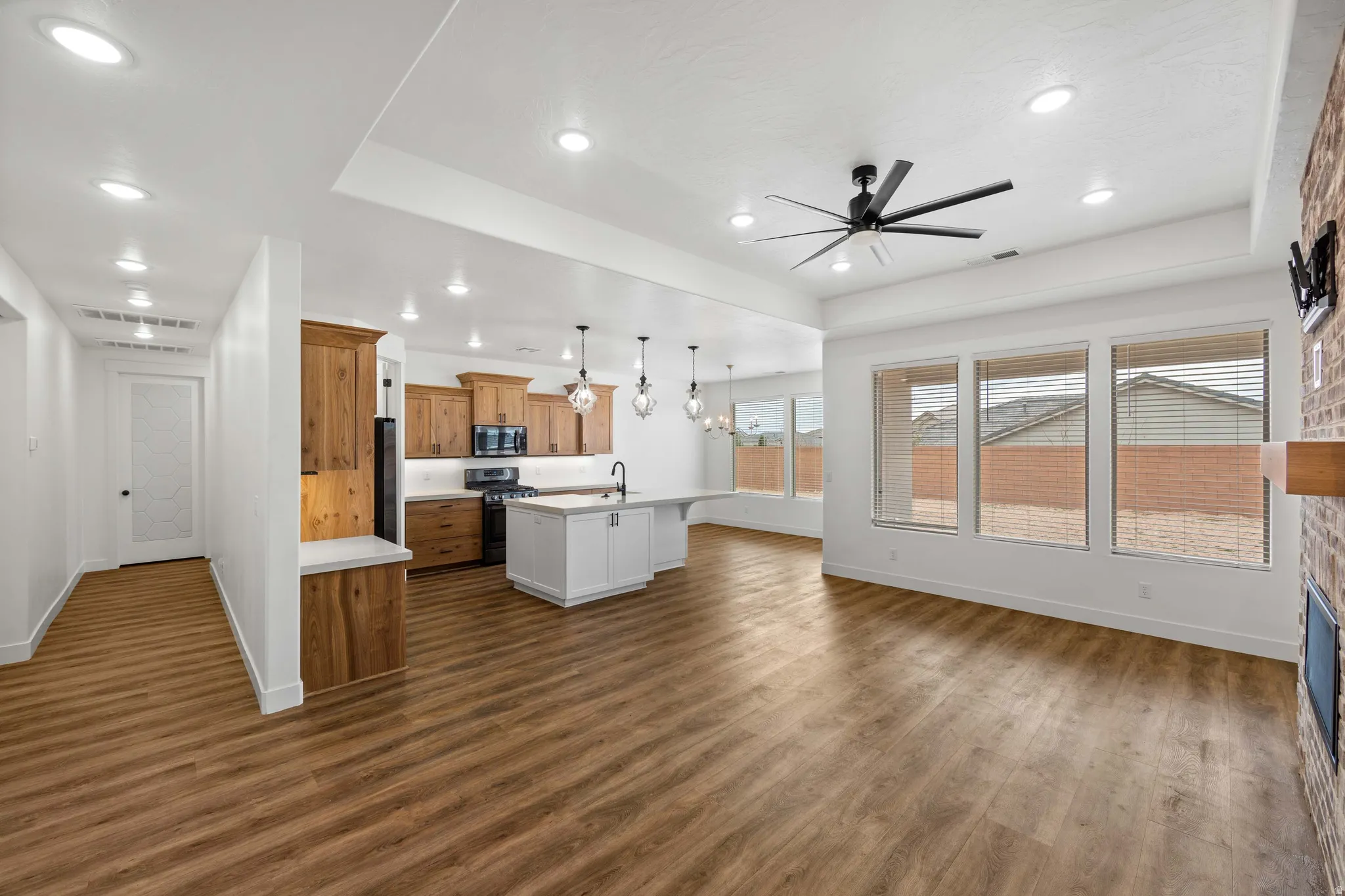 Kitchen with light countertops, wood finish cabinetry, ceiling fan, suspended lighting, and a kitchen island with sink