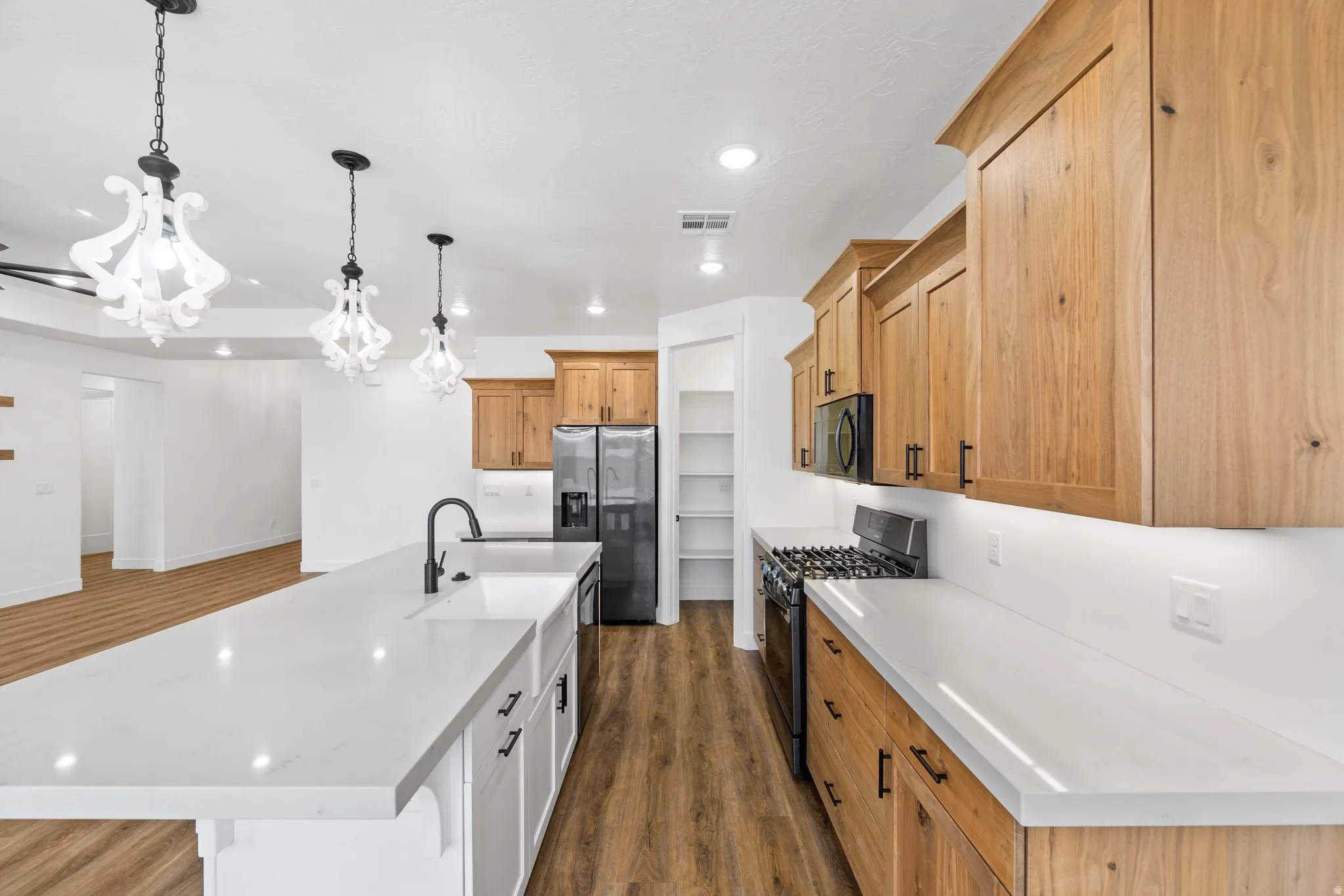 Kitchen featuring a spacious island, black appliances, dark wood-style flooring, decorative light fixtures, and light stone counters