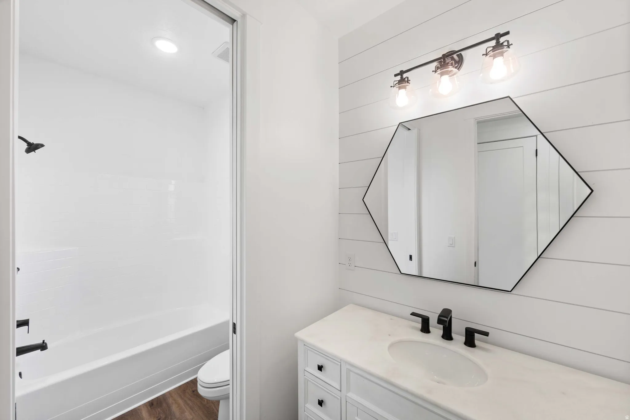 Bathroom featuring vanity, wooden walls, washtub / shower combination, and dark wood-style flooring