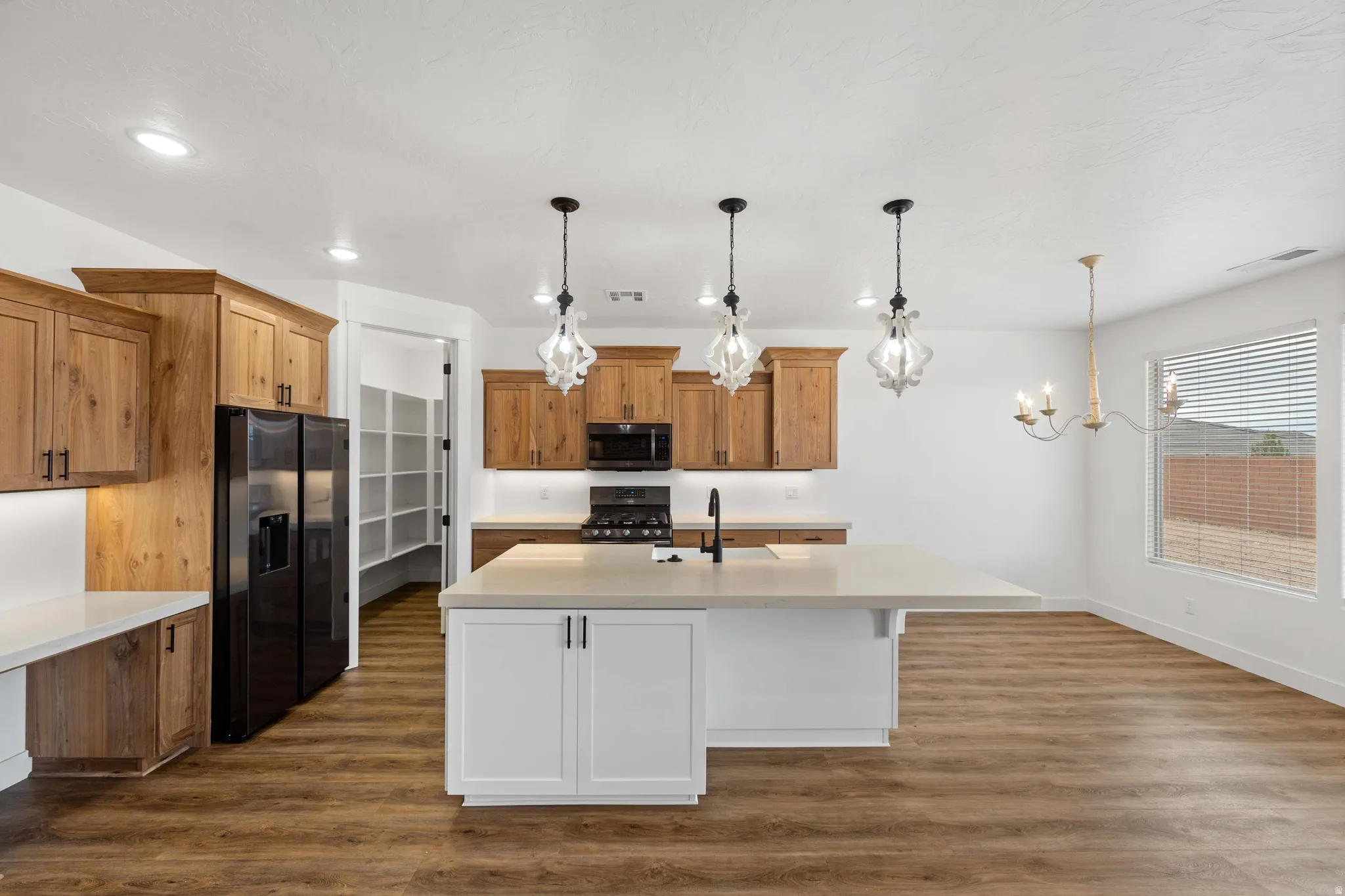 Dual tone kitchen with dark wood-type flooring, black fridge with ice dispenser, two tone color scheme, an island with sink, and gas range
