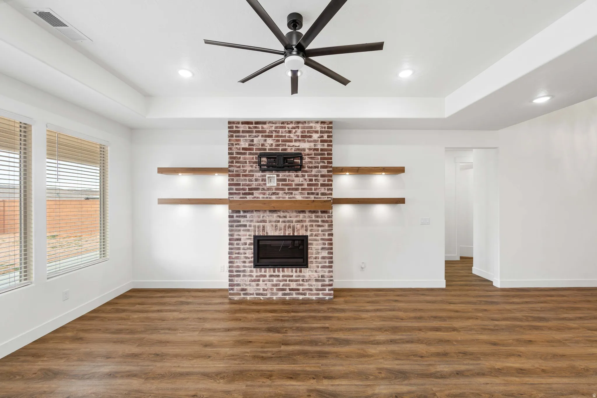 Unfurnished living room with dark wood-type flooring, ceiling fan, a fireplace, a tray ceiling, and recessed lighting