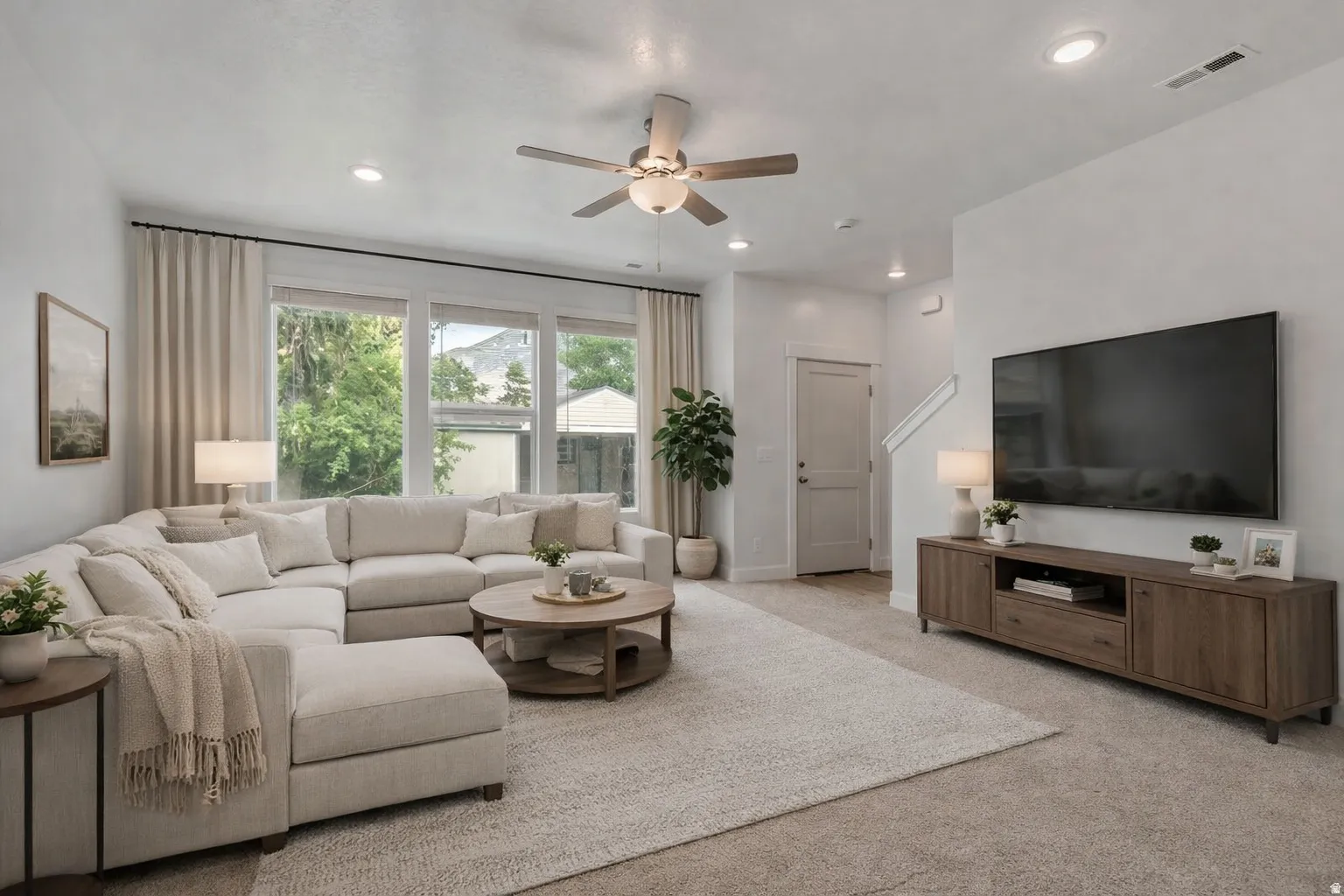 Bright living area featuring recessed lighting, a ceiling fan, large windows with neutral curtains, and light-colored carpeting