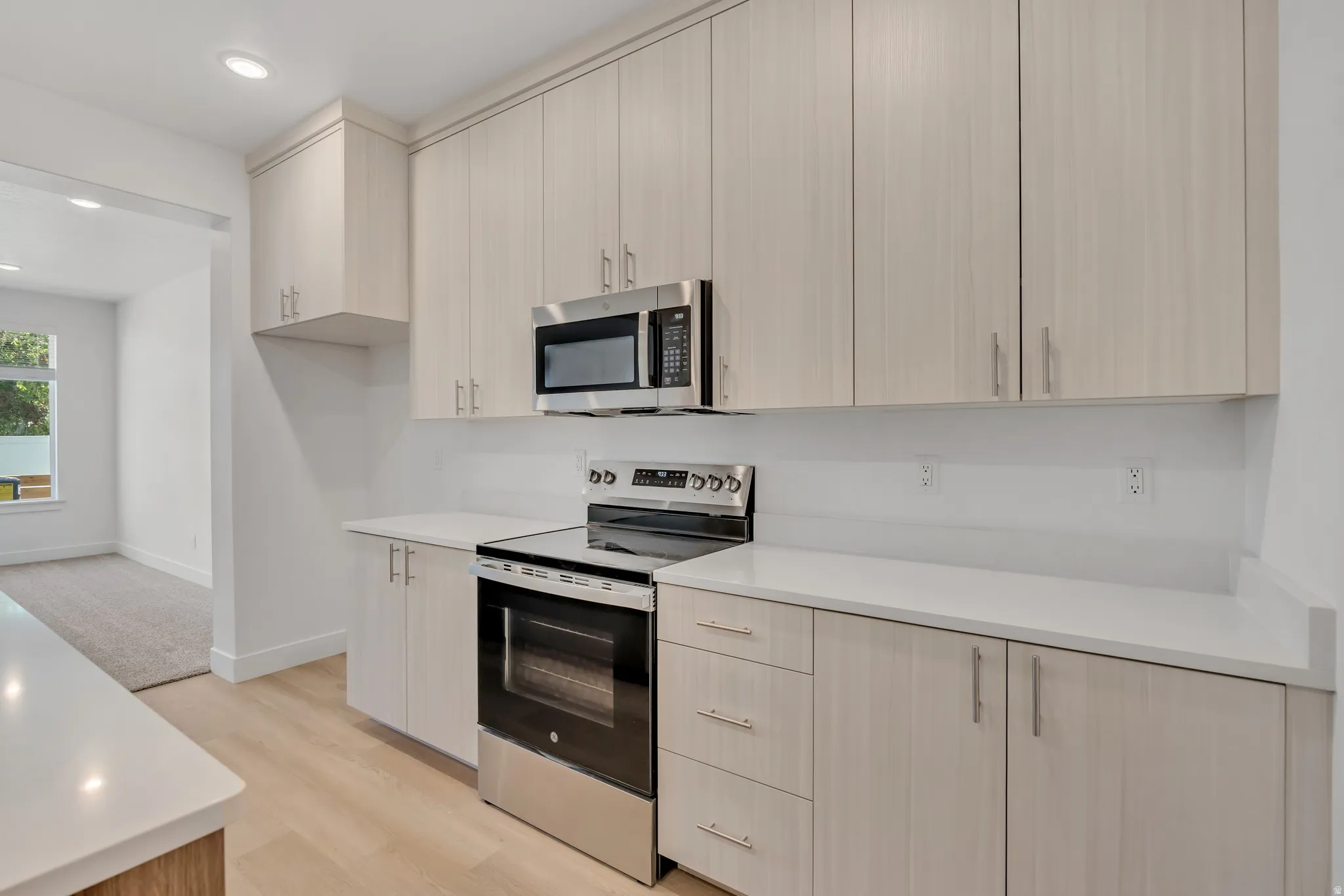Contemporary kitchen featuring light wood-finish cabinetry, stainless steel appliances, white countertops, and recessed lighting
