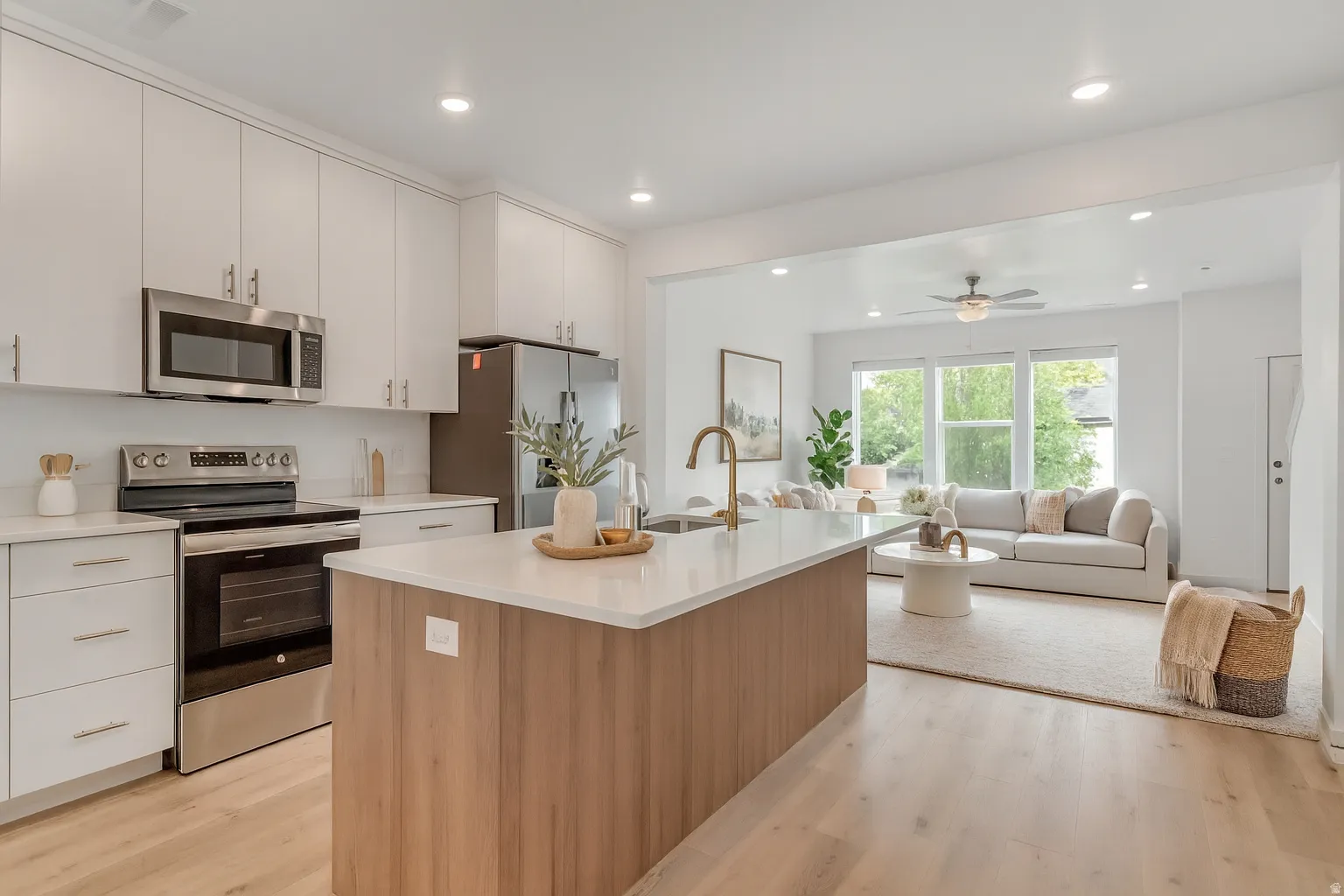 Open-concept kitchen featuring white cabinetry, stainless steel appliances, a wood-finish island with a light-toned countertop, and light wood-finish flooring