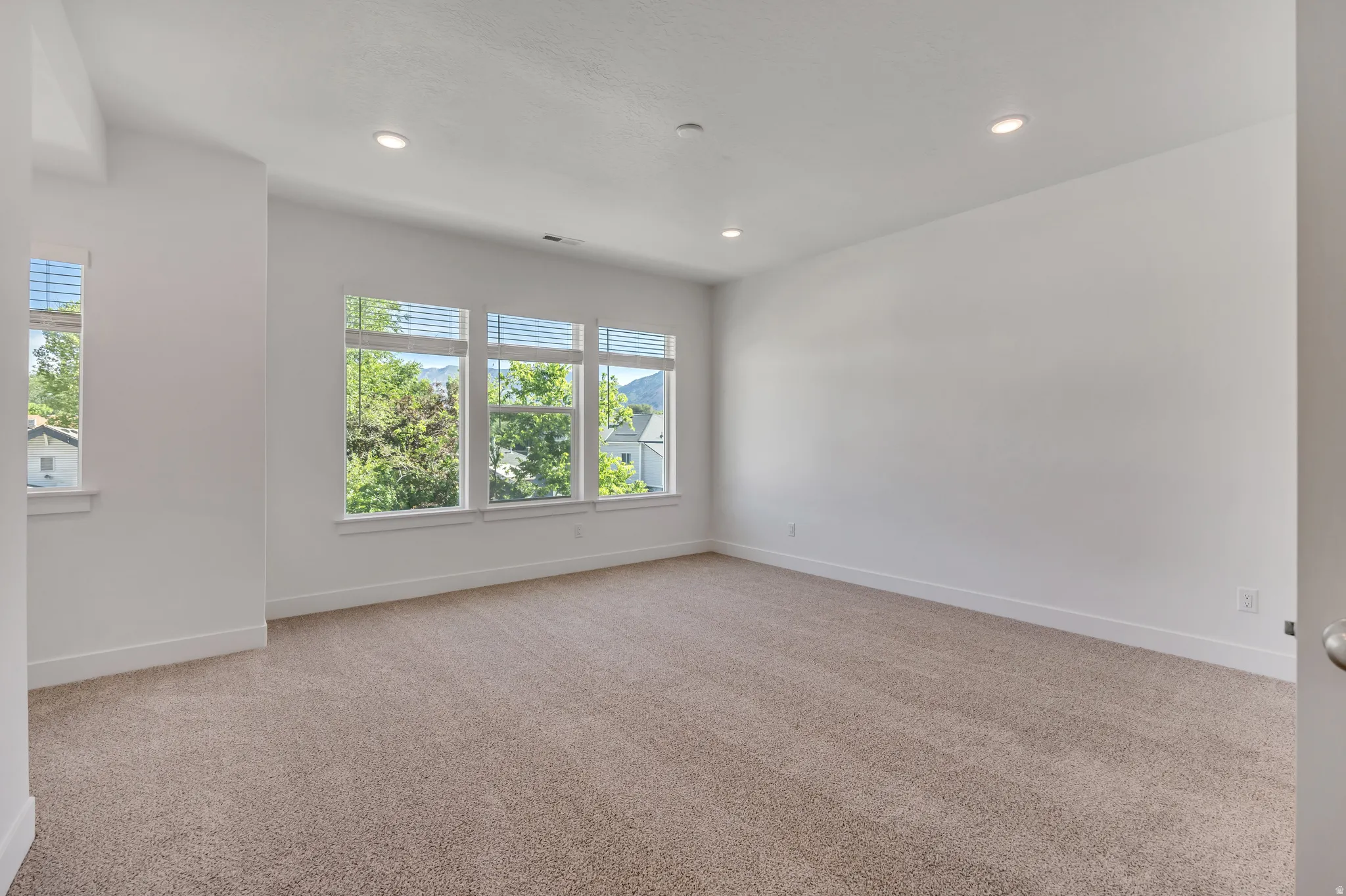 Spacious room featuring multiple windows, recessed lighting, and neutral-tone carpeting