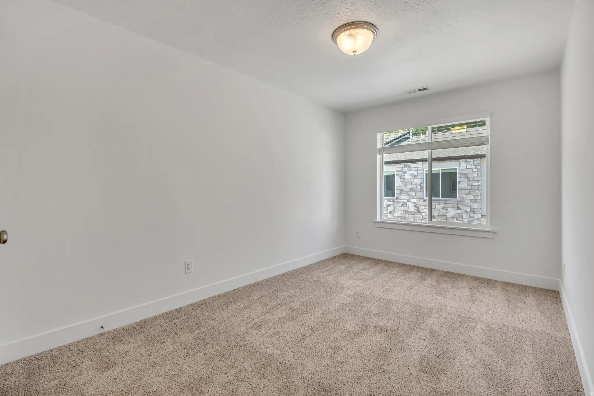 Neutral tone carpeted room featuring white walls, a large window with blinds, and a flush mount ceiling light fixture