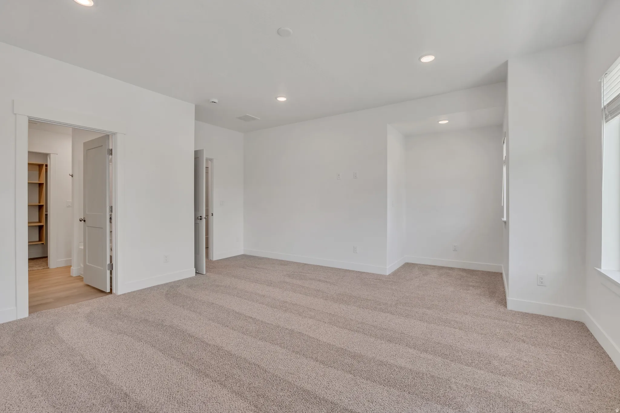 Spacious room featuring neutral carpeting, recessed lighting, white walls, and a window with blinds