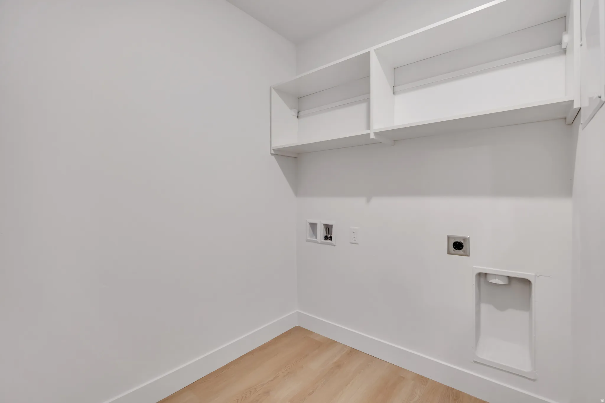 Dedicated laundry area featuring light wood-finish flooring, white walls, and built-in shelving