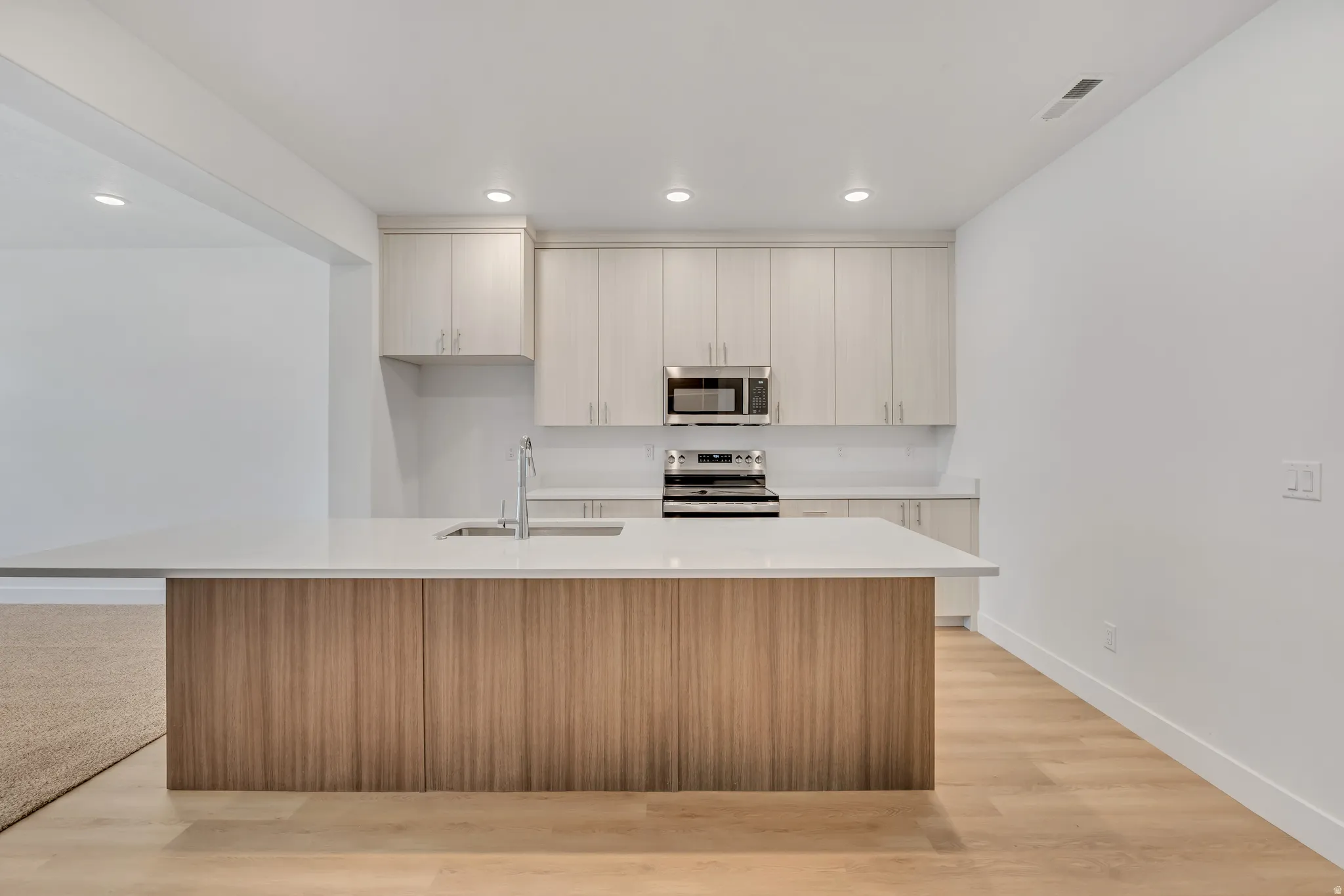 Kitchen featuring a large central island with a light wood-finish base and a light-toned countertop, stainless steel appliances, upper and lower cabinetry, and recessed lighting