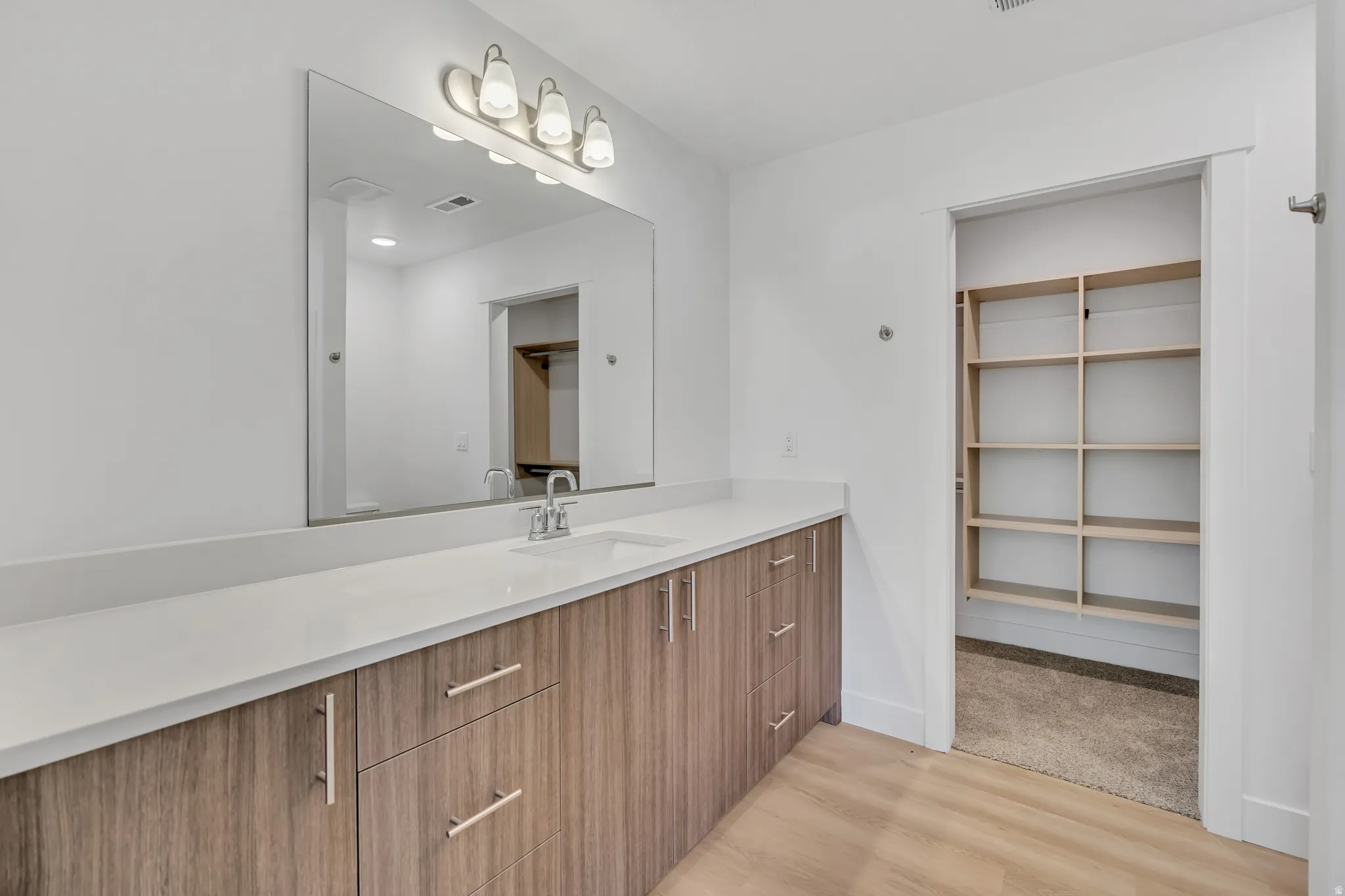 Contemporary bathroom vanity with a single undermount sink, light-colored countertop, and wood-finish cabinetry featuring brushed nickel hardware